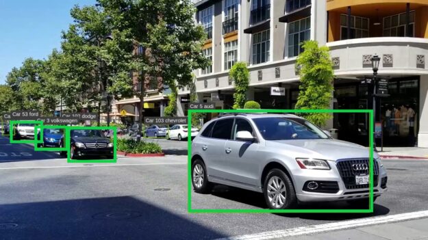 Photo of street with cars in green bounding boxes. Car in front has the largest bounding box as it's closest.