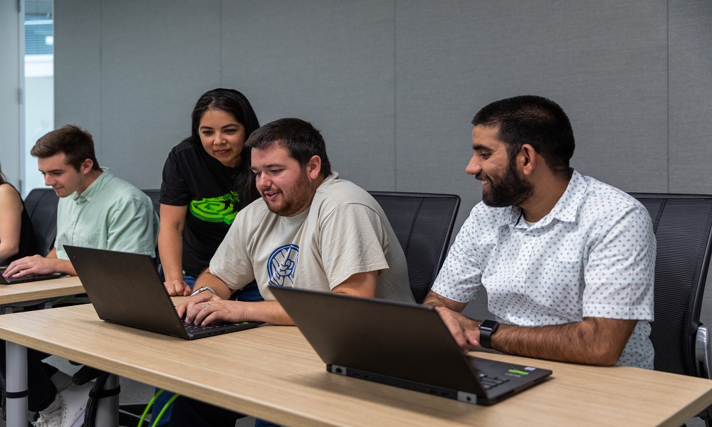 4 people sitting around laptops in an office.