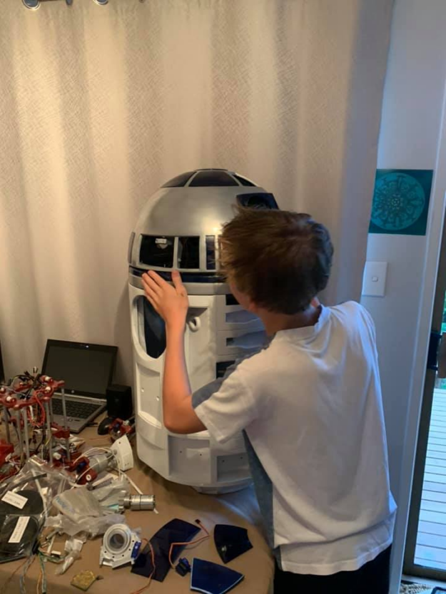 In the image, John’s son is working on inserting components onto the R2D2 incomplete frame to finalize the build of its head. 
