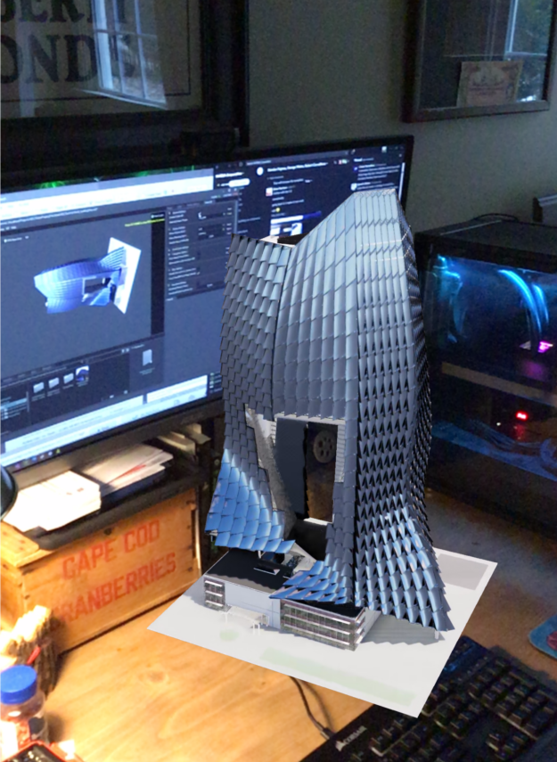 A 3D model of a skyscraper sits on a desk, viewed using AR mode.