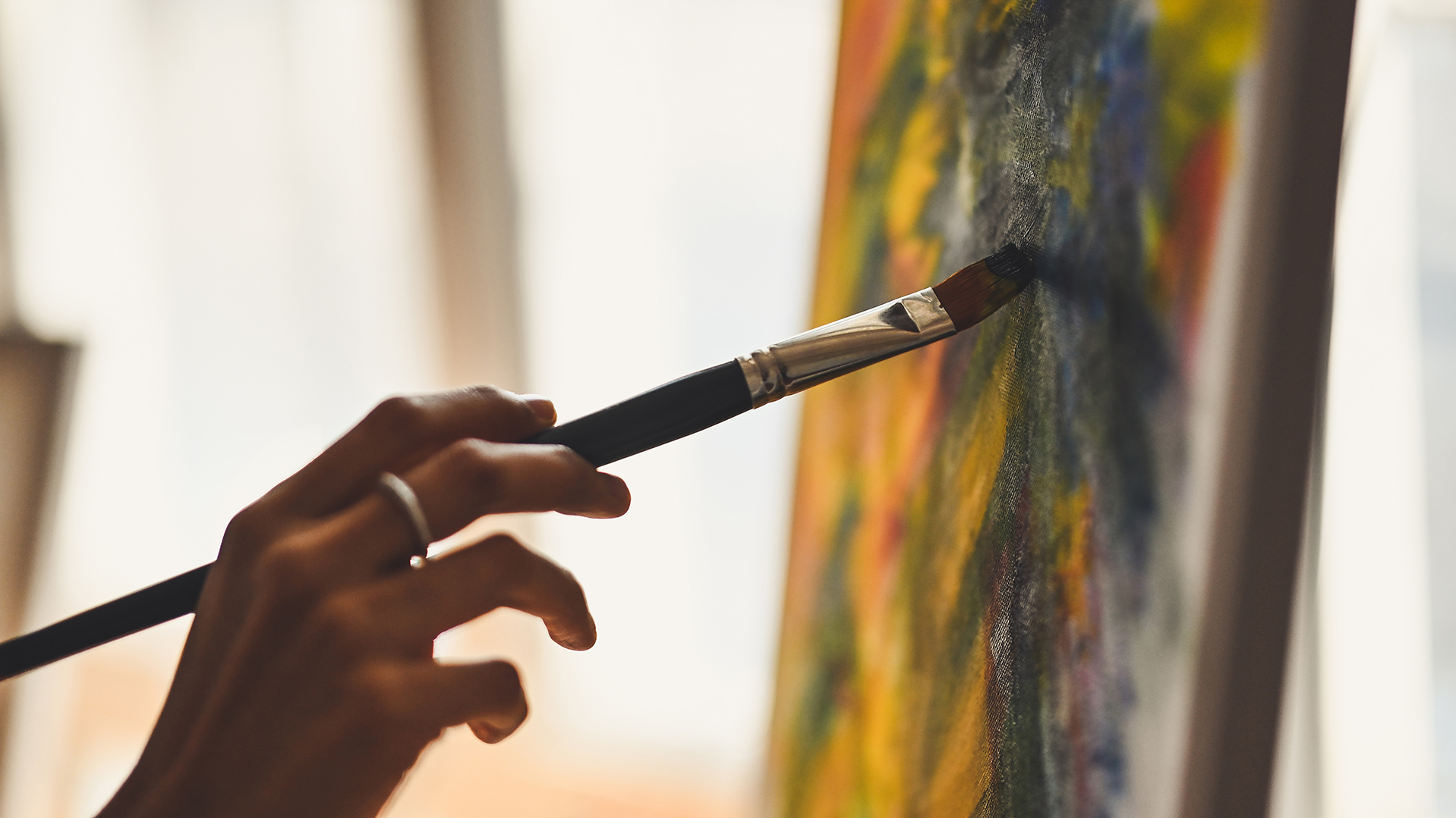 An up close view of a person holding a paintbrush and painting on a canvas.