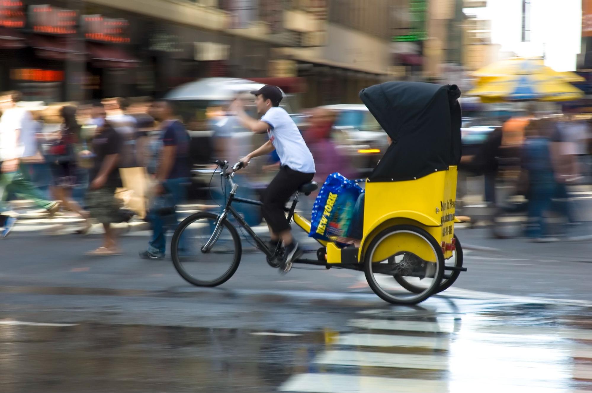 Photograph of an individual pedicab driver riding in the city.