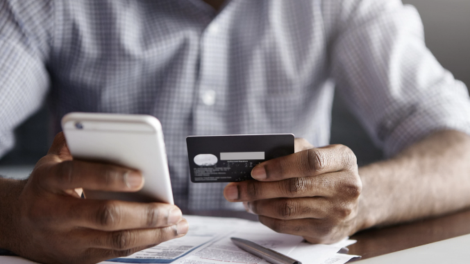 Person holding a smartphone and a credit card over some papers.