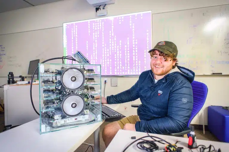 Picture of the student sitting next to a baby supercomputer on a desk.