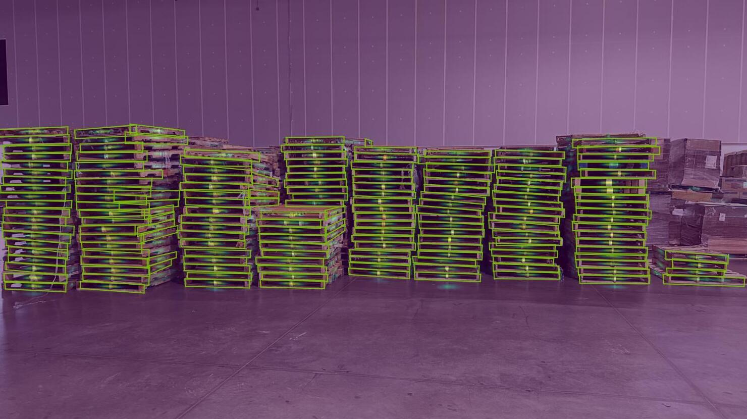An image showing nearly 100 pallets, some of varied shape, stacked in a warehouse.  The model detects each pallet except a few in the background. 