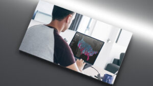 Photo at a skewed angle of person looking at a monitor that has graphics on it, against a grey background.