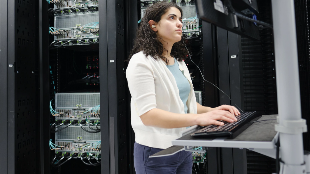 Photo of a person standing at a computer terminal in a data center.