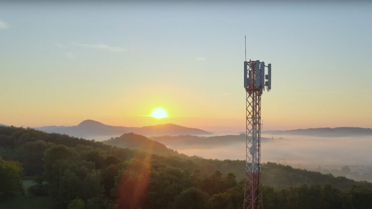 Photo of a cell tower at sunset among hills with fog.