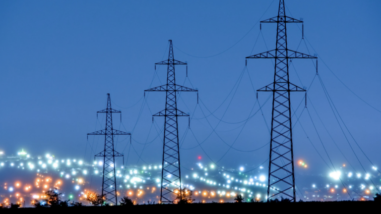 Photo of a power line against city lights at twilight.