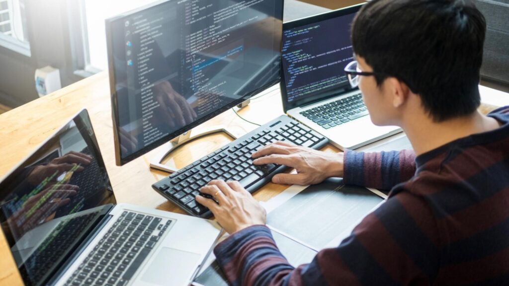 A person typing in front of several computer monitors.